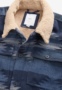 Námořnická a krémová flanelová košile s límcem z měkkého, plyšového materiálu a dvěma náprsními kapsami. Má geometrický vzor a černé knoflíkové zapínání.