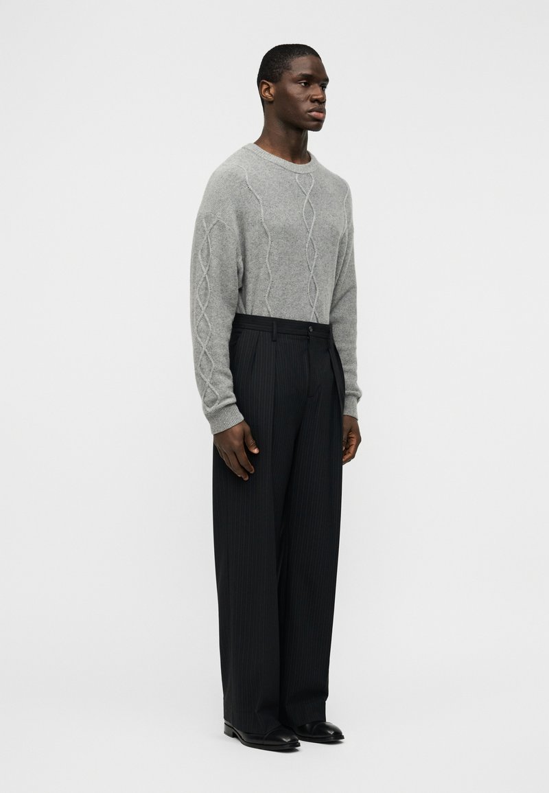 Gray knitted sweater with cable pattern, paired with black pleated trousers. The trousers have a straight fit and are accented with a black belt.