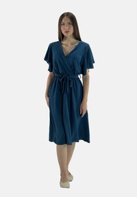 Türkisfarbenes Wickelkleid mit kurzen, schwingenden Ärmeln, V-Ausschnitt und einem Stoffgürtel. Knielang, aus weichem, strukturiertem Material.
