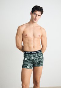 Schwarze und grüne Boxershorts mit wiederholtem "HUGO"-Textmuster. Elastischer Bund mit "HUGO"-Logo. Hergestellt aus dehnbarem Stoff.