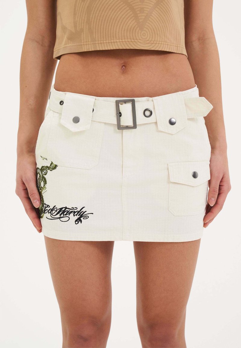 Mini gonna in denim bianco con vita a cintura, tasche frontali e intricate ricami neri e verdi con un design grafico.