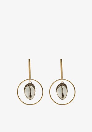 Złote kolczyki w formie kółek z zawieszką w kształcie białej muszli, z misterną teksturą i detalami, zawieszone na teksturowanym pręcie.