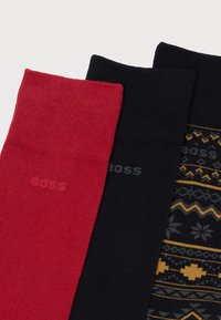 Drei Paar Socken in Rot, einfarbig Schwarz und gemustert Dunkelblau mit gelben Akzenten. Mit gerippter Textur und sichtbarem Logo.