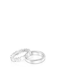 Dos anillos de plata, uno con una banda sencilla con la inscripción "TOUS S925" y el otro con pequeños eslabones en forma de oso conectados, sobre un fondo blanco.