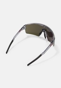 Gafas de sol con un diseño sin montura, lentes tintados de color gris oscuro y brazos de plástico transparente con puntas de goma negra. Apariencia ligera y deportiva.