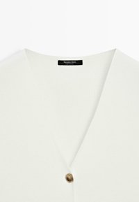 Witte V-hals top met een enkele bruine knoop en een Massimo Dutti label bij de hals, gemaakt in China.