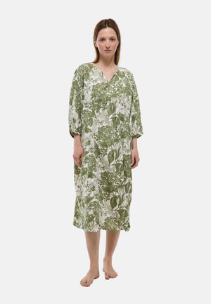 Femme debout pieds nus portant une robe ample à imprimé floral vert et blanc longueur genou, avec des manches trois-quarts et un col en V.