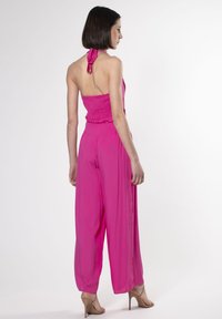 Tuta fucsia con corpino arricciato, collo all'americana e pantaloni a gamba larga. Tessuto morbido e dettagli arricciati in vita.