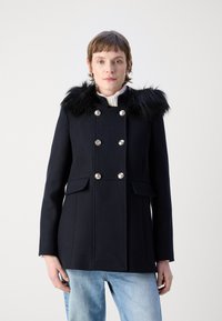 Juodas vilnos mišinys paltas su dirbtiniu kailio apykakle, dvigubos sagos stiliaus, sidabrinės sagos ir šoninės kišenės. Yra priderinta siluetas.