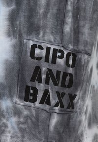 Tie-dye t-shirt i nuancer af grå og blå, med et sort stofmærke hvor "CIPO AND BAXX" er tydeligt vist. Blød tekstur.