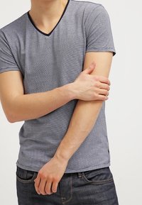 Marinblå og grå stribet V-hals T-shirt, korte ærmer, blødt stof, tætsiddende pasform, med marinblå kant omkring halsudskæringen og detalje ved sidesømmen.