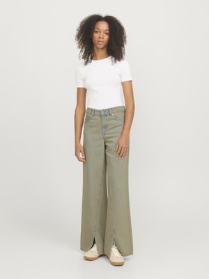 Hellgrüne, weite Jeans mit einem Frontschlitz, hoher Taille und klassischer Denim-Textur. Kombiniert mit einem eng anliegenden weißen T-Shirt und beigen Turnschuhen.