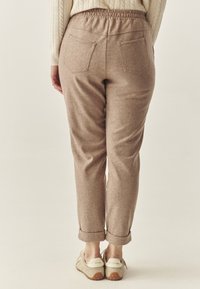Light brown, elastic-waist pants with a tapered fit, two back pockets, and rolled cuffs, made from a soft, textured fabric.