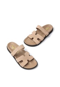 Beige Wildledersandalen mit zwei breiten Riemen, die ein ausgeschnittenes Schriftzugdesign zeigen, einer weichen Fußbettn und einer schwarzen Gummisohle für guten Halt.