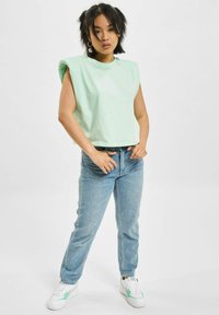 Mintgrønn, kortermet topp uten ermer med skulderputer, kombinert med lyseblå denimjeans og hvite sneakers med grønne detaljer.