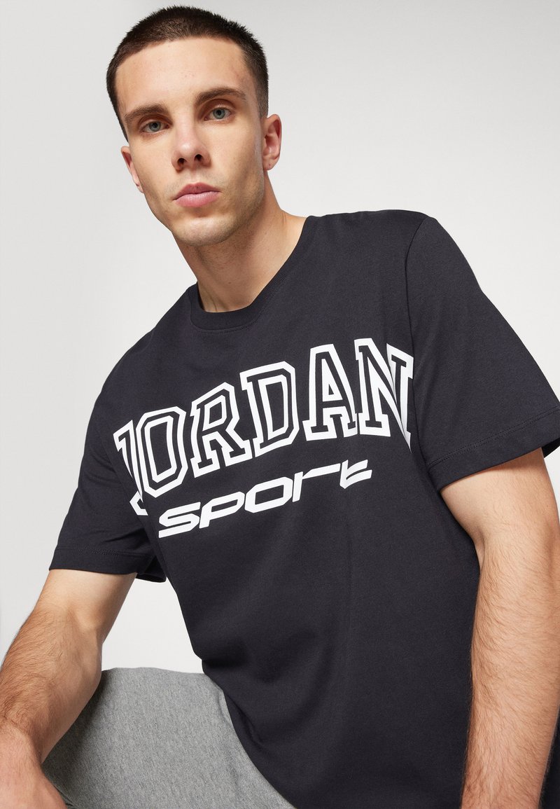 Camiseta de algodón negra con el texto en blanco "JORDAN" en negrita y "SPORT" debajo. Mangas cortas y un cuello redondo clásico.