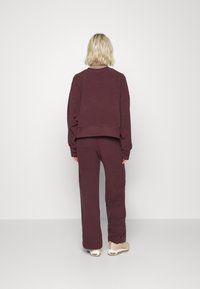 Burgundy fleece sweatshirt med croppad design, matchande byxor. Strukturerad tyg och avslappnad passform. Skorna har en ljusbeige färg.