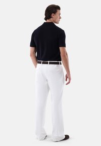 Polo shirt blu navy a maniche corte, abbinato a pantaloni bianchi e una cintura marrone. Il tessuto sembra liscio e leggero.