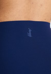 Tamno plavi rastezljivi pojas od tkanine s suptilnim otisnutim logotipom, glatke teksture i bez vidljivih šavova. Idealan za sportsku ili udobnu odjeću.