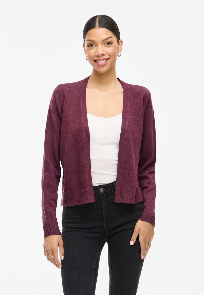 Burgundy open-front cardigan made of soft knit material, featuring long sleeves and ribbed cuffs, paired with a white top and black jeans.