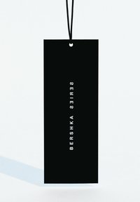 Black rectangular tag with a hole for string, featuring the text "BERSHKA SERIES" in white vertical lettering on one side.