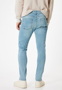 Ljusblå denimjeans med smal passform, fem fickor och subtila blekningar. Har hög midja och klassisk knappstängning.