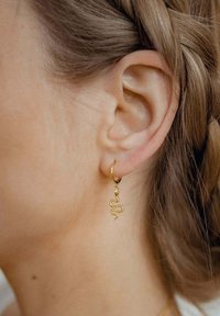 Pendiente de aro dorado con un charm de serpiente colgante. La serpiente presenta una superficie texturizada y un detallado intrincado. Apto para orejas perforadas.