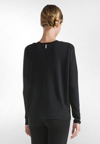 Schwarzes Langarmshirt aus weichem Stoff, mit rundem Halsausschnitt und lockerer Passform. Tag im Nackenbereich sichtbar.
