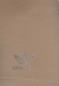 Tissu sportif beige avec un logo Adidas en strass agrémenté d'un design de trèfle. Texture lisse, coupe ajustée.
