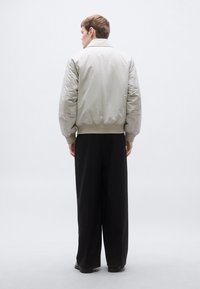 Επένδυση μπουφάν bomber σε ανοιχτό γκρι, με ριμπ τελείωμα και μανσέτες. Συνδυάζεται με φαρδιά μαύρη παντελόνια. Ομαλή υφή.