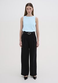 Top fără mâneci de un albastru deschis, cu textură ribbed, purtat cu pantaloni negri cu talie înaltă și picioare largi, împreună cu o curea neagră cu cataramă metalică.