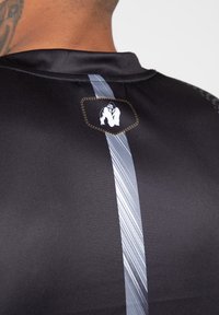 Zwarte sportshirt met een gladde textuur, met een centrale grijze streep en een logopatch met een gestileerde gorilla.