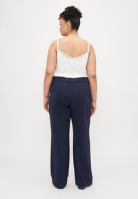 Biały top na ramiączkach z koronkowym wykończeniem, zestawiony z granatowymi spodniami na elastycznej talii. Spodnie są luźne i sięgają do podłogi.