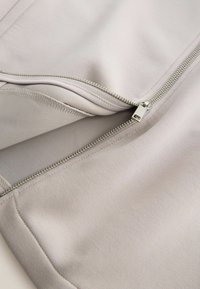 Light gray fabric with a smooth texture, featuring a silver zipper at the edge. The zipper is partially open, revealing the inner layer.