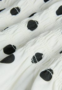 Valge kangas, millel on kogutud tekstuur ja ühtlaselt paigutatud mustad tammetõru-kujulised mustrid kogu ulatuses.