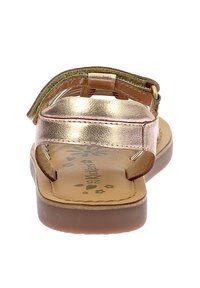 Sandaña metálica dorada de punta cerrada con correa ajustable, plantilla acolchada marrón y detalles florales en la suela.