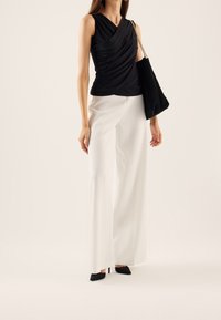Top negro sin mangas con un diseño drapeado, combinado con pantalones de pierna ancha blancos de cintura alta y tacones negros de punta. Incluye un bolso negro de hombro.