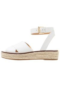 Valkoiset nahkainen espadrille-sandaalit, joissa on ristikkäinen yläosa, nilkkavöitä, kultainen solki ja kudottu juuttipohja.