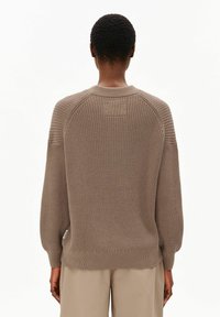 Khakifarbener Strickpullover mit strukturiertem Design, Raglanärmeln und gerippten Bündchen, mit einem kleinen Etikett an der Seite.