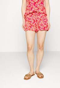Top de tanque floral rosa e calções a condizer, com um corte solto e tecido leve. Sandálias casuais em tom de pele com detalhes em dourado completam o look.