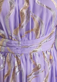 Robe lilas avec des motifs ondulés métalliques en argent et en or. Tissu doux et fluide avec des détails de taille froncée et une jupe plissée.