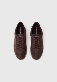 Baskets en suede marron avec des orteils arrondis, des lacets marron contrastants et une semelle en caoutchouc beige clair. Présente la marque "Calvin Klein" sur la languette.