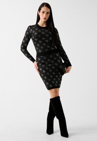 Czarna sukienka z długim rękawem o dopasowanym kroju, z geometrycznym wzorem w kolorze srebrnym i miękkiej dzianiny. Połączona z czarnymi kozakami za kolano.