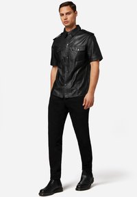 Zwarte leren short-sleeve shirt met twee voorzakken, drukknoopsluitingen en schouderaccenten. Gecombineerd met zwarte slim-fit broek en laarzen.