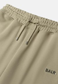 Pantaloni della tuta beige con vita elastica e cordino. Presenta un piccolo logo nero "BALR." sul frontale. Tessuto morbido e texture.