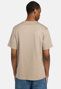 Beige Baumwoll-T-Shirt mit Rundhalsausschnitt und kurzen Ärmeln, das eine glatte Textur aufweist. Die Rückansicht zeigt eine lockere Passform und ein schlichtes Design.