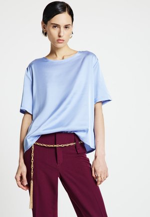 Top in raso azzurro chiaro con vestibilità rilassata, scollo rotondo e maniche corte, abbinato a pantaloni color bordeaux con cintura a catena dorata.