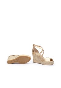 Sandalias de cuña metálicas doradas con puntera descubierta, correas de tobillo entrelazadas y una plantilla de yute trenzado. Suela de goma texturizada para mayor agarre.