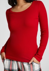 Rode langmouwtop van ribstof met een ronde hals. Gecombineerd met geruite pyjamabroek in rood, groen en wit.