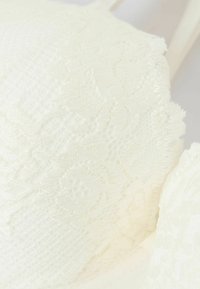 Spetsbralette i mjuk vit, med ett texturerat blommönster, släta kanter och tunna justerbara band.